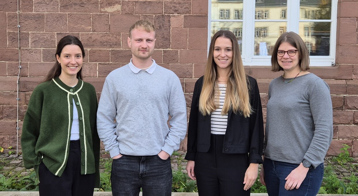 Eine Gruppe von drei Frauen und einem Mann stehen für ein Foto vor einem Fenster.